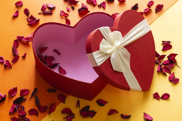 open heart shaped box with dried petals flowers on colorful background