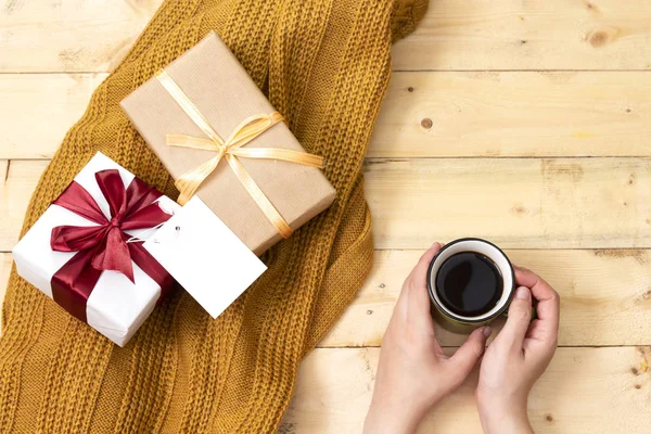 hand holding coffee cup and gift box, empty card above woolen scarf on wooden table  hello winter and christmas concept