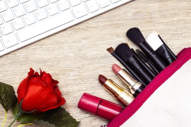 Makyaj çantası farklı renkte ruj ve ahşap arka planda pembe ojeli çeşitli fırça içerir.