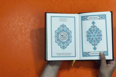 El ele tutuşup kutsal Kur 'an' ı Arapça kaligrafi ile turuncu arka planda izole etmek.