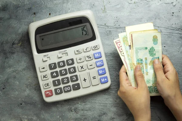 Cezayir resmi para birimini (Cezayir dinarı) tutan ve saymak için büyük gri bir hesap makinesi kullanan yakın çekim elleri 