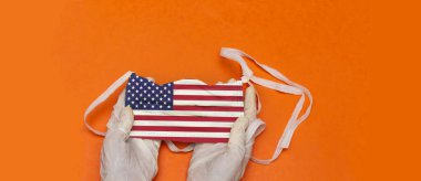 Tıbbi eldivenli kadın elleri Amerikan bayrağıyla tıbbi maske tutuyor. ABD 'de salgın hastalık konsepti. Coronavirüs salgınının niteliği