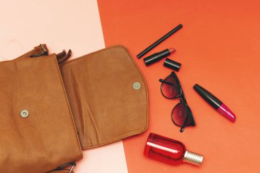 Ruj ve rimel fırçası, şişe parfümü güneş gözlüğü ve göz kalemi ve pembe ve kırmızı kağıtta omuz çantası.