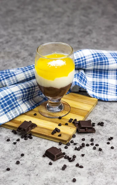Homemade layered vegan dessert of baked coconut cream and chocolate and orange, lemon fruit in glass jar on wooden board decorated with chocolate chips