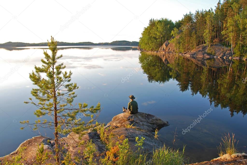 Man sitting at still Saimaa lake in Finland at sunset