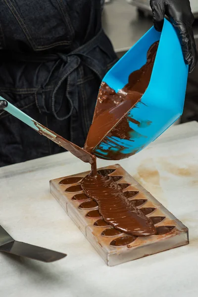 Confeiteiro em luvas faz chocolates em formas — Fotografia de Stock