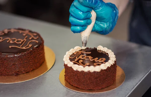 Confectioner makes chocolate cake with icing and cream