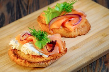 Tahta kesme tahtasındaki balık ve sebzeli sandviç.