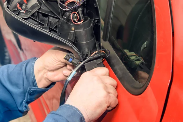 Mechanic repairing a rearview mirror of a red car, car service workshop