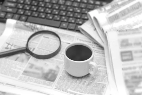 Newspaper, magnifier, cup of coffee and laptop. A pile of daily newspapers with news Headlines. Modern gadgets and old magazines.