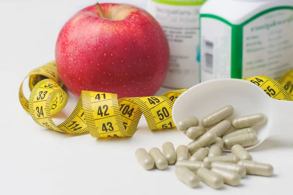 Multivitamin capsules, food Supplement on a white spoon, fresh red Apple, measuring tape as a dietary food concept.