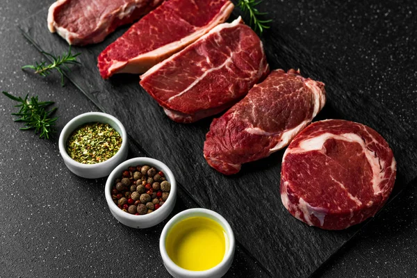 Urval av rå nötkött kött mat biffar mot svart sten bakgrund. — Stockfoto