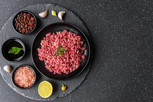 Fresh minced meat ground beef on a black plate against stone background.