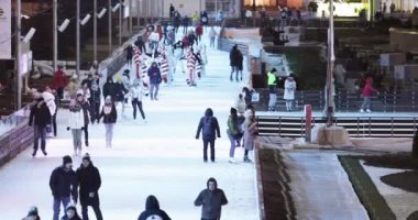 Arka planda buz pateni pisti ziyaretçileri, sahne ve Noel süslemeleri.