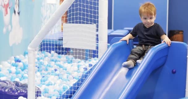 Menino infantil joga em um slide de plástico — Vídeo de Stock