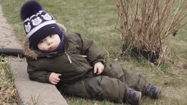 Мальчик в комбинезоне лежит на траве — стоковое видео
