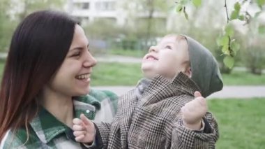Palto giyen çocuk yapraklarla oynuyor.