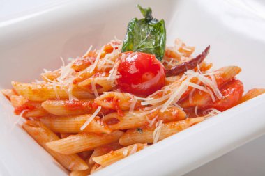 Derin beyaz bir tabak içinde Parmesan peyniri serpilir domates soslu Penne makarna
