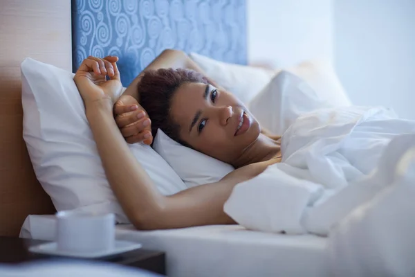 Bir yatakta yatan genç mutlu siyah kadın.