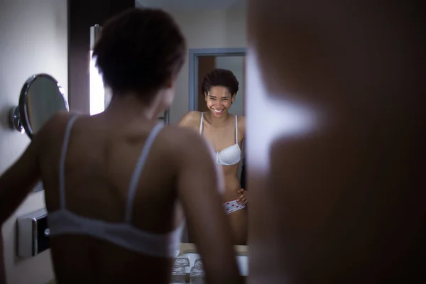 Молодая черная красивая девушка в белых трусах восхищается собой в зеркале — стоковое фото