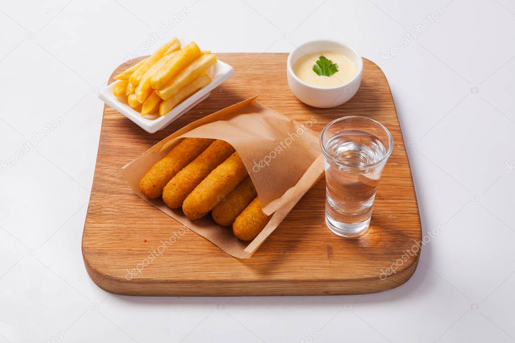Fish sticks on a wooden board with sauce and fried potatoes