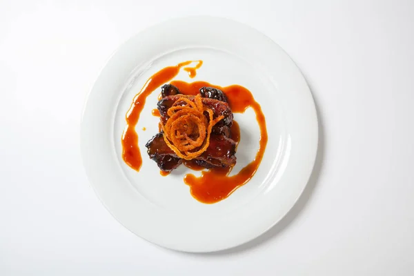 Jugoso trozo de cordero bajo salsa roja dulce y cubierto con cebolla frita en gran plato redondo blanco sobre fondo blanco . — Foto de Stock