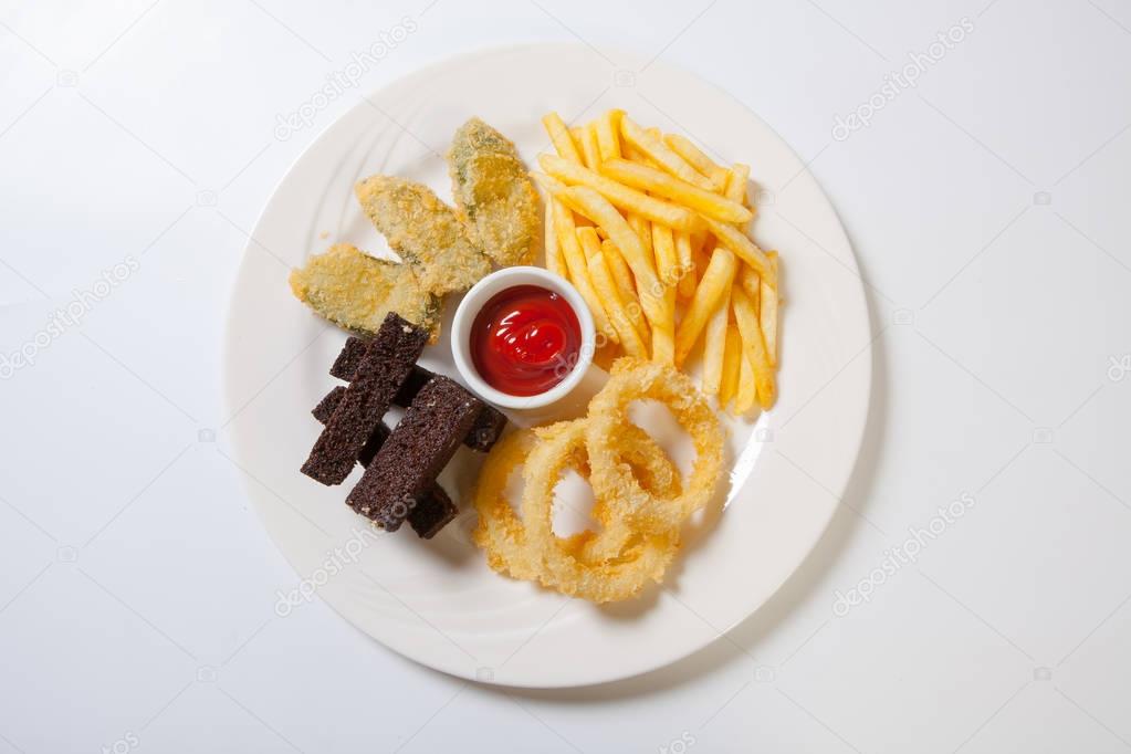 Fresh beer snacks assortment on a white plate. French fries, croutons and zucchini and onion rings.