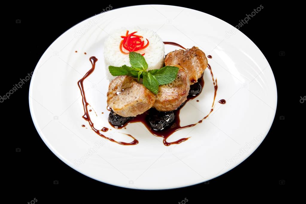 Pork medallions steak with prunes sauce on a white plate