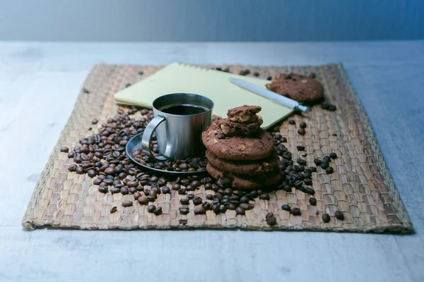 Šálek kávy a kávových zrn na dřevěný stůl s cookies a Poznámkový blok — Stock fotografie