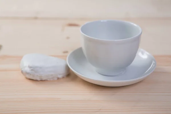 Una taza de cerámica blanca pura y platillo y pan de jengibre se encuentra en una mesa de madera — Foto de Stock