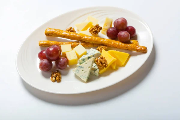 Сыр и орехи, и виноград на белой тарелке — стоковое фото