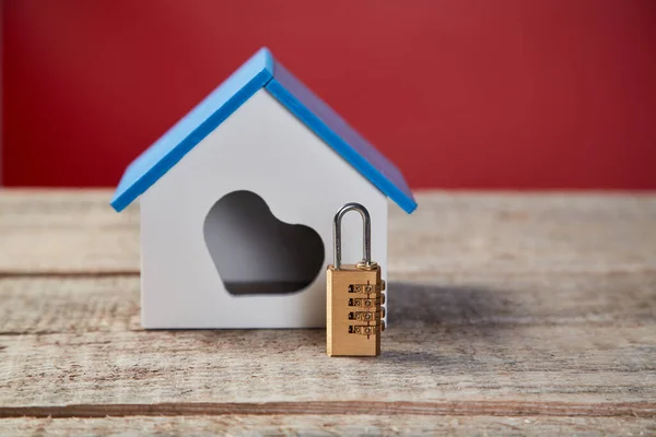 Family home security. Real estate, property safety system. House with heart symbol and combination lock on wooden surface.