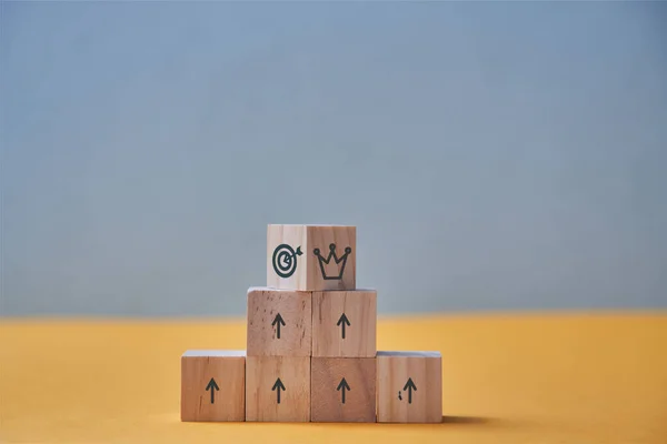 Negocios y crecimiento profesional. Logro de metas, carrera profesional. Pirámide de bloques de madera, la corona y los signos de destino en la parte superior — Foto de Stock