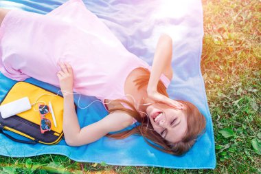 Müzik akışı. Medya eğlencesi. Güzel bir kadının parkta çimlerde dinlenip müzik dinlemesi, eğlenmesi.