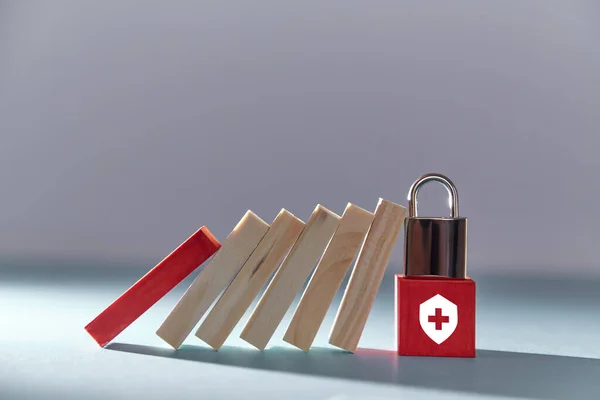 Cubo rosso con cartello medico, lucchetto sopra. Tavole domino cadenti. Garanzia di risarcimento, indennizzo. Copia spazio — Foto Stock