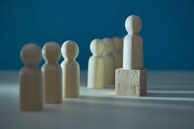 Tahta figür küpün üzerinde duruyor. Karanlık arka planda minyatür ve lider insanlar. Liderlik ve üstünlük kavramı