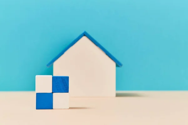 Model of house miniature on blurred background. Square of wooden cubes in white, blue colours. Mockup style. Copy space