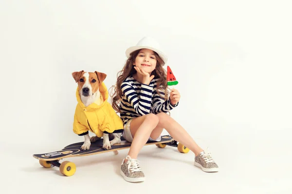 Girl is siting with her dog on skateboard