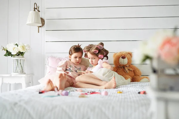 Dos chicas están tumbadas en la cama mirando fijamente el teléfono inteligente — Foto de Stock