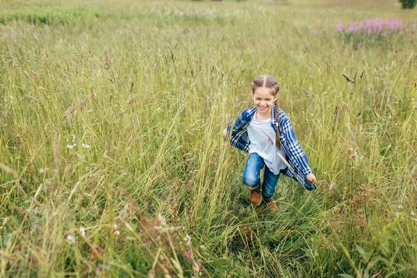 Crianças, felicidade e conceito de relaxamento. Menina bonita com cabelos longos, sorrindo amplamente enquanto corria na grama verde do campo, desfrutando de momentos agradáveis inesquecíveis na bela natureza — Fotografia de Stock