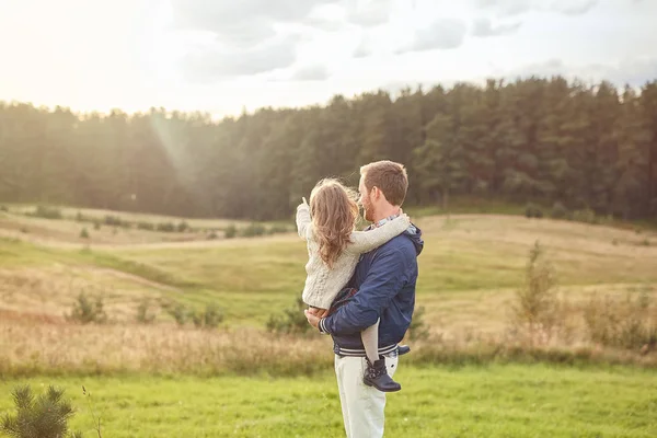 Маленькая очаровательная девочка, находящаяся на руках его отца, указывающая своим грибком на большой лес, желая пойти туда. Отец и дочь, прогуливаясь по полю, чувствуя расслабление, наслаждаясь спокойной атмосферой — стоковое фото