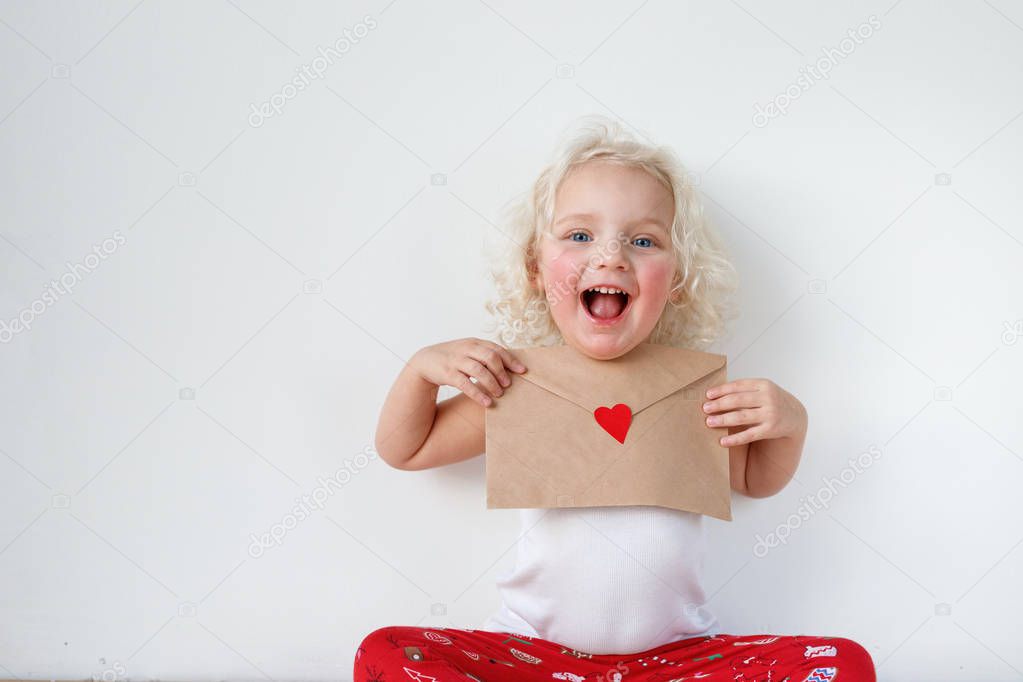 Portrait of adorable small kid has cheerful expression, holds letter to Santa Claus, hopes her dreams come true, isolated over white background. Cheerful little child with letter. Beauty and childhood