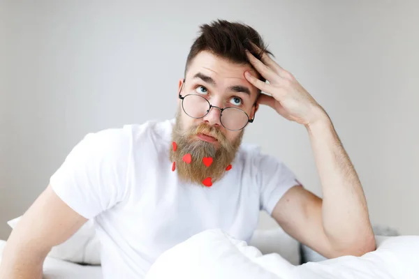 Thoughtful bearded male with trendy hairstyle, mustache and beard, looks pensively upwards through spectacles, plans his working schedule, awakes in morning, finds necessary solution in mind.