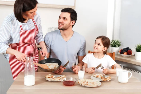 Photo of hard working wife, husband and their daughter sit together at kitchen table, going to eat delicious pancakes, enjoy togetherness. Friendly family eat breakfast, appetizing flannel cake. — Stock Photo, Image