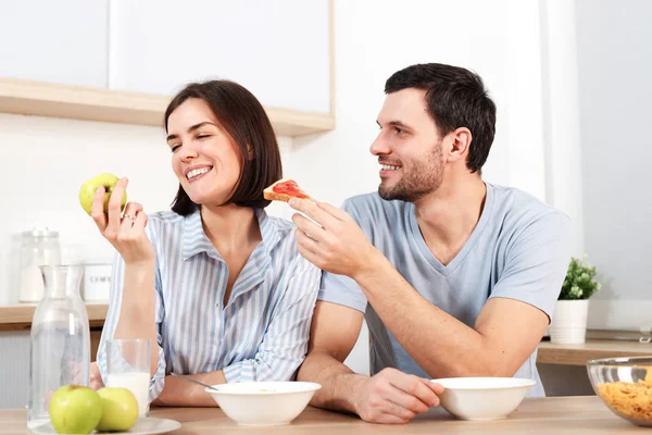Счастливая пара проводит свободное время или выходные вместе на кухне, счастливый муж предлагает жене перекусить, она отказывается, так как ест зеленое яблоко, завтракает. Концепция семьи, приготовления пищи и отношений . — стоковое фото
