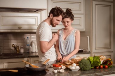 Kadın ve erkek vegeterians birlikte mutfak iç karşı durup, sebze salata hazırlayın. Aile çift üzerinde rahat mutfak pişirmek, kocası genç karısı preapre akşam yemeği için tüm aile için yardımcı olur.