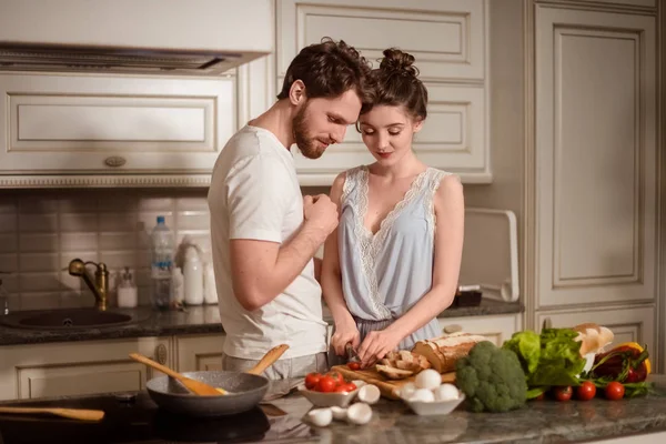 Os vegeterians femininos e masculinos unem-se contra o interior de cozinha, preparam a salada vegetal. Família casal cozinheiro na cozinha aconchegante, marido ajuda jovem esposa a preparar o jantar para toda a família . Imagem De Stock