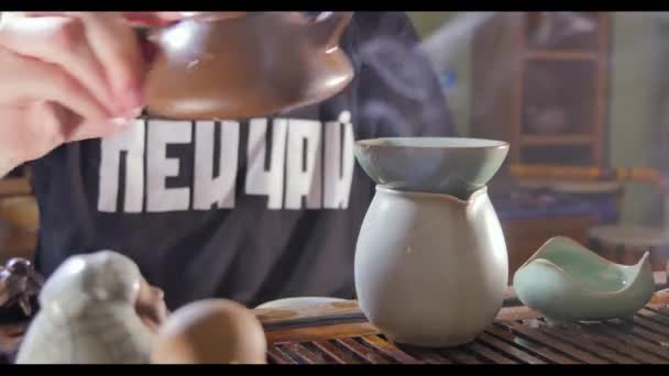 Traditionele Chinese theeceremonie en giet de thee in een glas van de klei theepot thee stromen in cup op bruine achtergrond. Thee uit de theepot In beker te gieten. Chinese thee ceremonie. Toon op het brouwen van groen — Stockvideo
