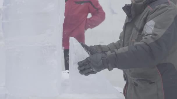 Operaio con una motosega intagliare una scultura di ghiaccio. Gli uomini discutono il lavoro con sculture di ghiaccio. I lavoratori puliscono la neve. Uomini che trasportano ghiaccio. I lavoratori trasportano ghiaccio e neve sulla macchina. Giobbe con ghiaccio e neve — Video Stock