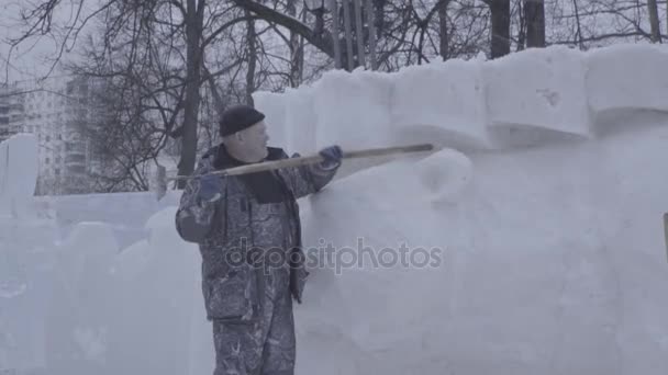 Hombre paleando nieve. Haz escultura hecha de nieve. Escultura de nieve, bloques apilados en espera de la escultura. Esculturas de nieve de animales en la iluminación artificial. Hombre con pala de nieve limpia aceras en — Vídeo de stock